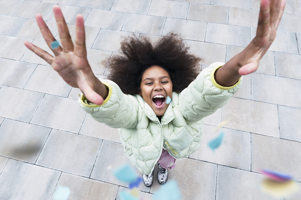 royalty-free, stock image, pau novell, Cheerful girl with arms raised standing amidst confetti falling on footpath