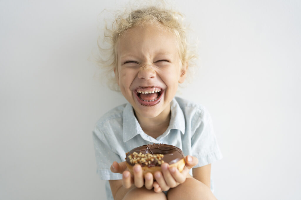 Stockfoto, lizenzfrei, Fröhliches blondes Mädchen hält Donut mit Schokolade und lacht, Svetlana Karner