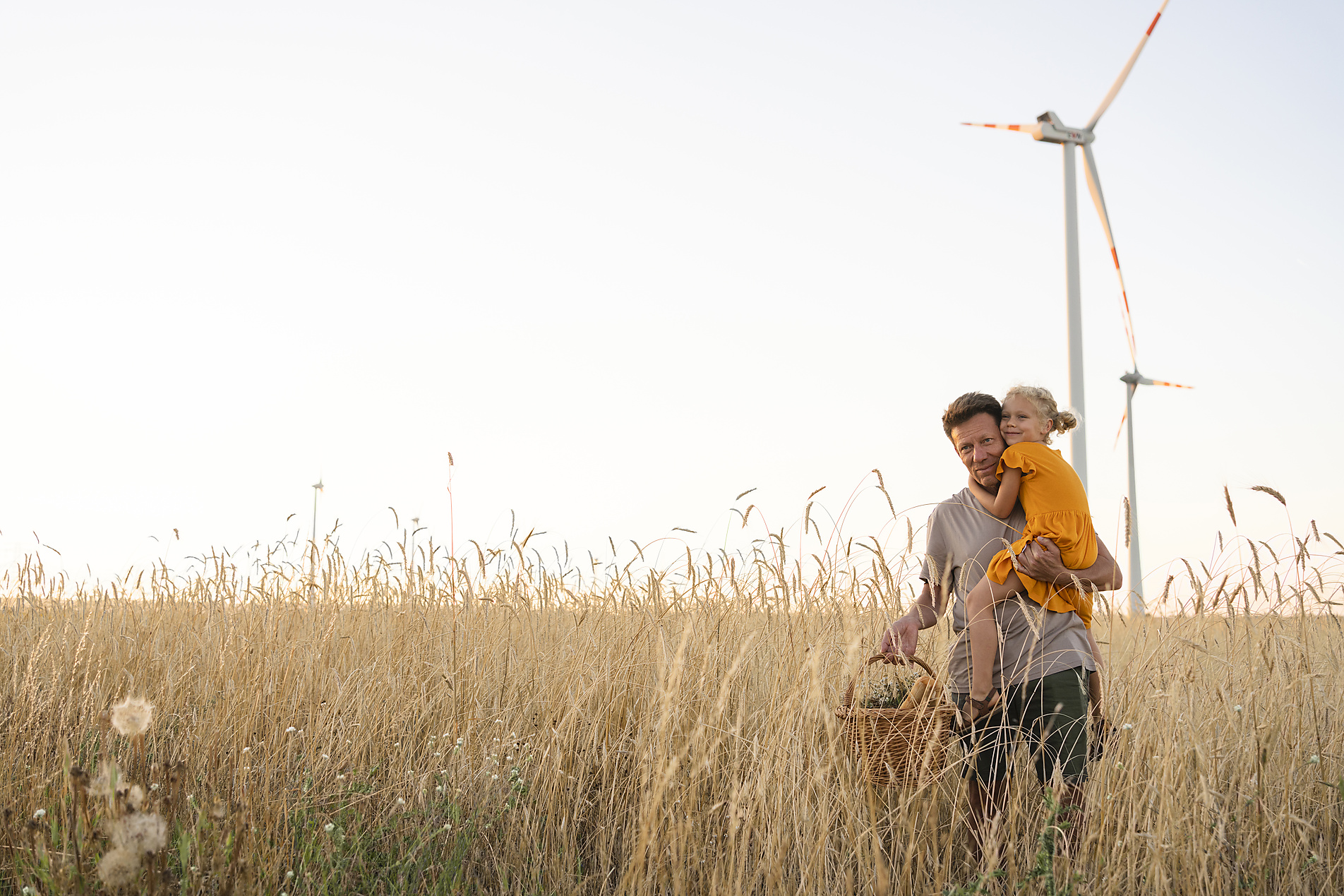 Stockfoto, lizenzfrei, Vater trägt Tochter auf einem Weizenfeld mit Windrädern, Svetlana Karner