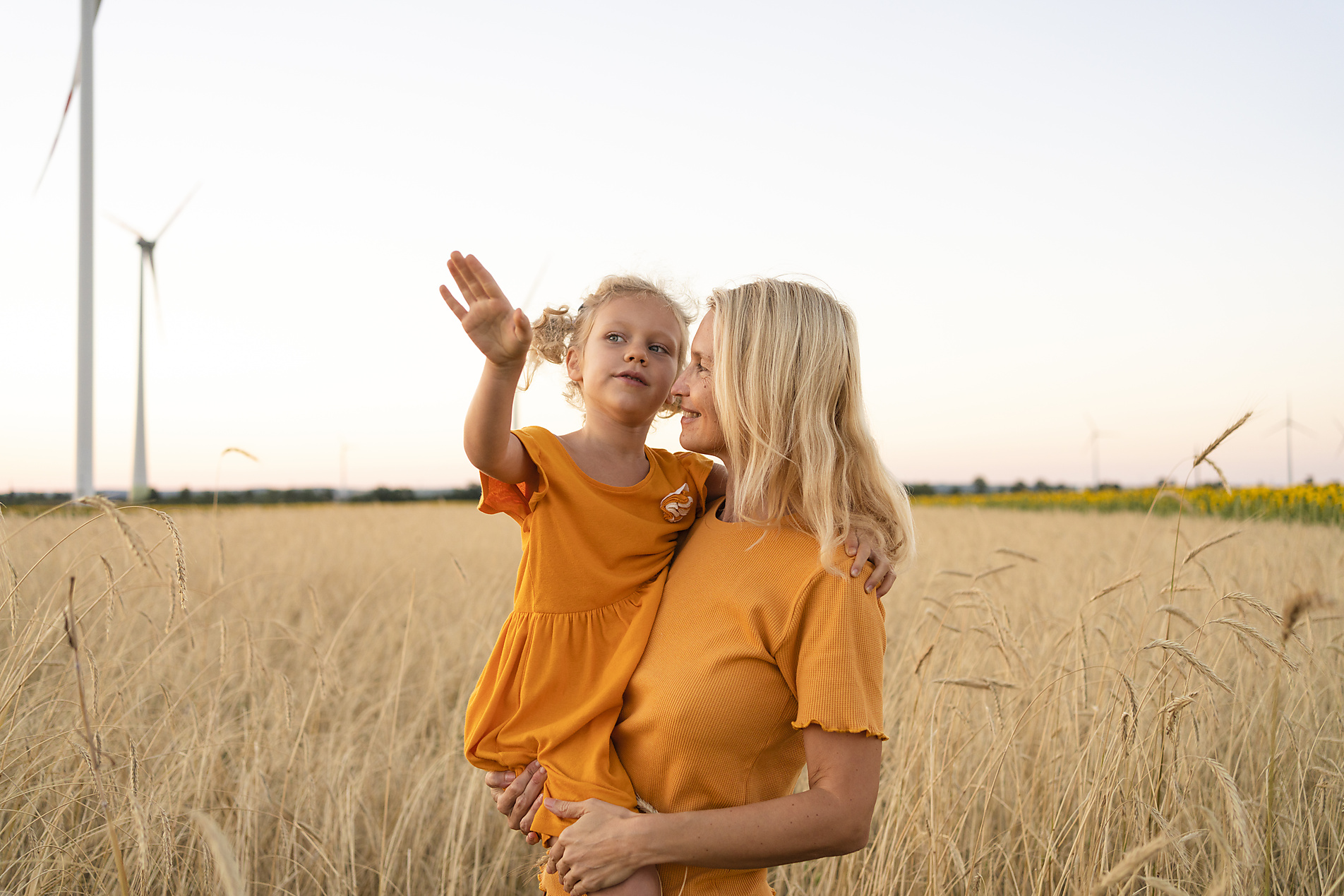 Stockfoto, lizenzfrei, Lächelnde Frau mit Tochter im Weizenfeld vor Windrädern, Svetlana Karner