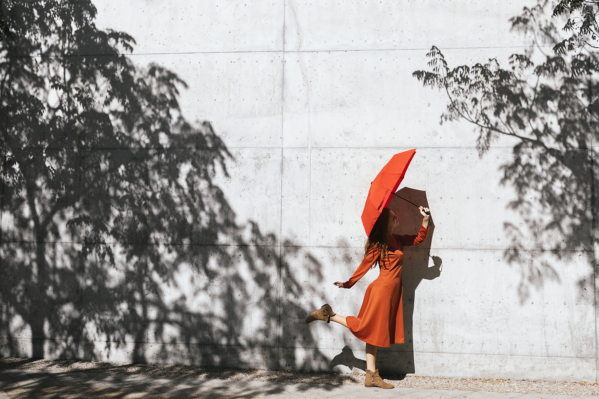 Stock image, royalty-free, Woman in red dress holding red umbrella while standing against tree shadow wall, Tania Cervian