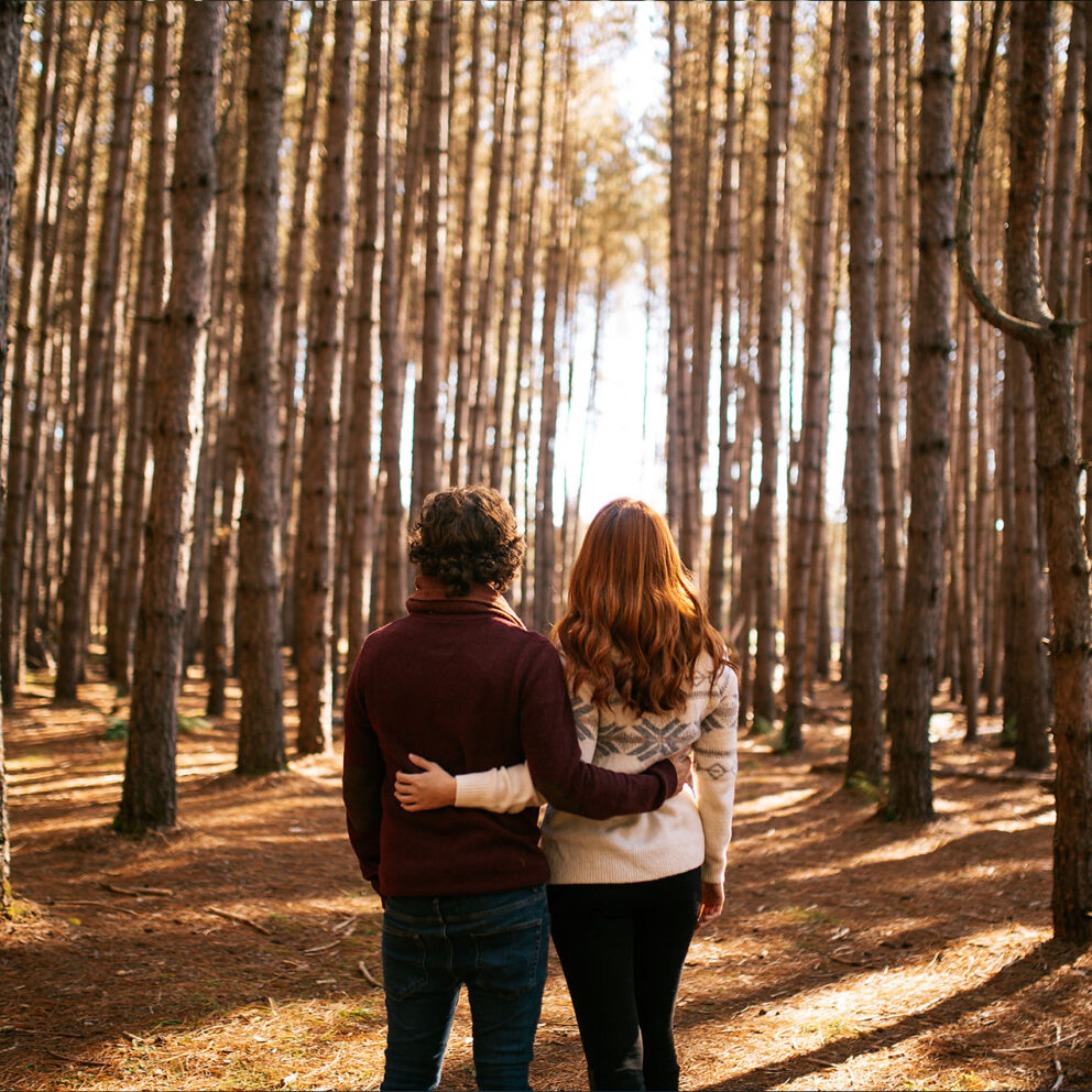 royalty-free, stock image, couple standing in forest in autumn arm in arm while looking at the sun, photographer Addictive Stock / Camille Girard