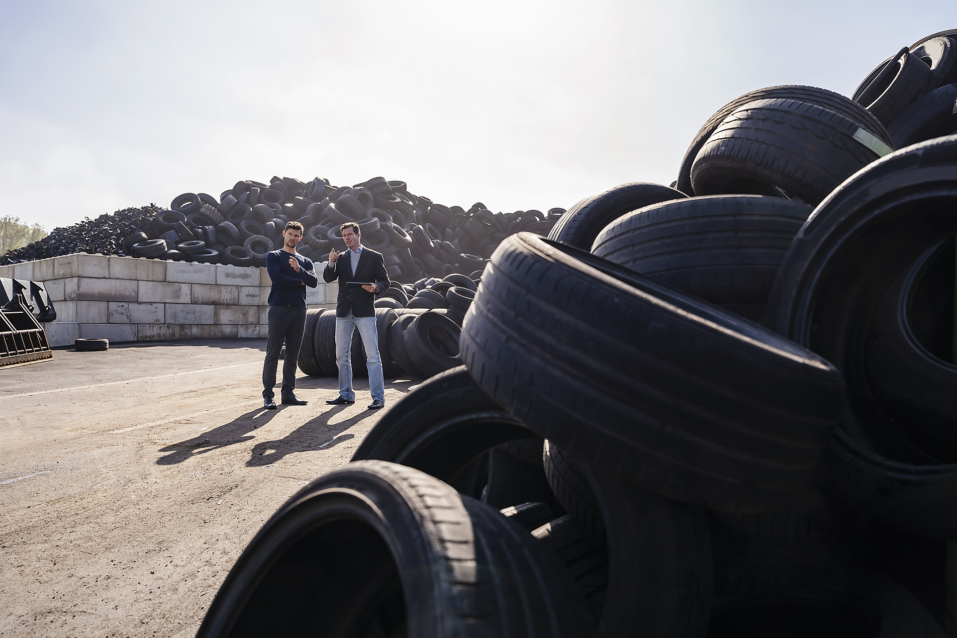 Stock image, royalty-free, Businessmen discussing over heap of rubber tires at recycling plant,Westend61, Pyrum Innovations, Recycling, Sustainability, eco-friendly, Industry, Daniel Ingold,