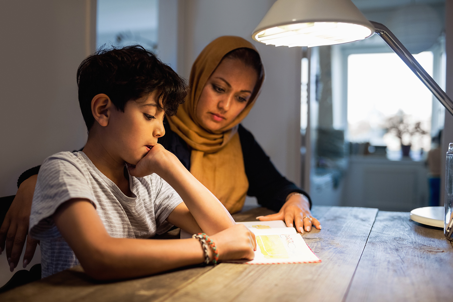 Stock image, royalty-free, Mother and son reading book under illuminated desk lamp at home, education, school, future, Westend61, Maskot Images