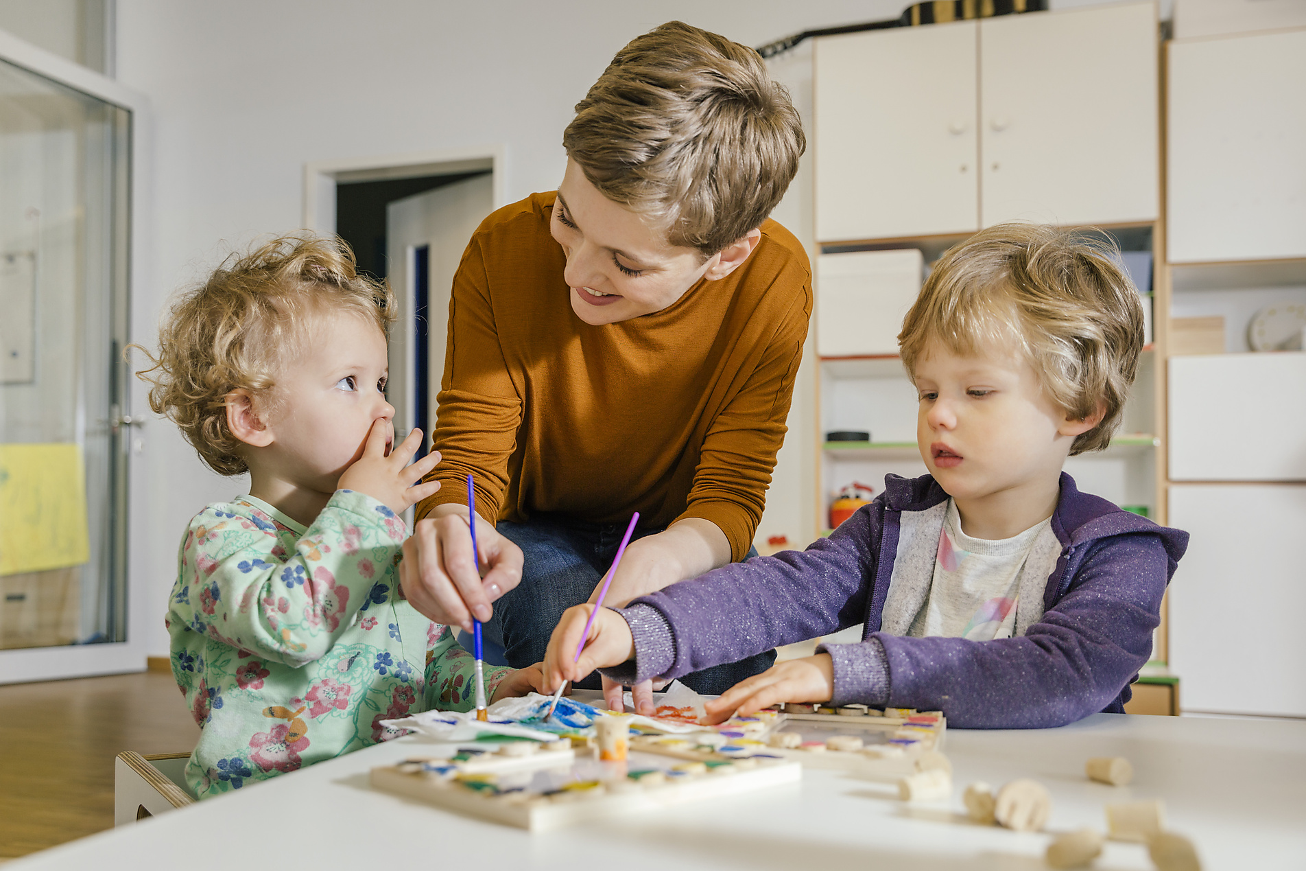 stock image, royalty-free, Mareen Fischinger, Westend61, Pre-school teacher painting with two children in kindergarten, education, future