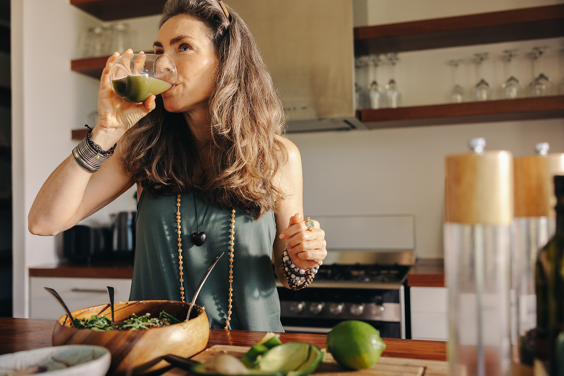 Vegan woman drinking some green juice while having a buddha bowl. Mature woman serving herself a healthy plant-based meal in her kitchen, stock image, royalty-free, plant based food, vegetarian, vegan, sustainable, healthy eating
