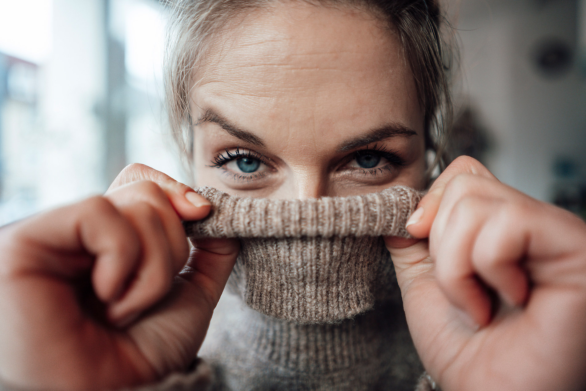 blonde woman hides behind her turtleneck but her eyes radiate joy and optimism, stock photo, royalty free, safety, comfort zone, me-time, insecurity competence