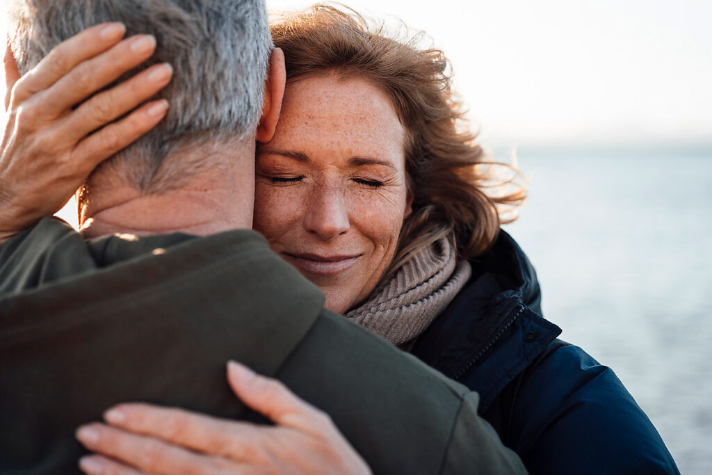 Smiling woman hugging her husband on the beach, security, insecurity skills, visual trends 2023, stock photo, royalty free, top 25 images security