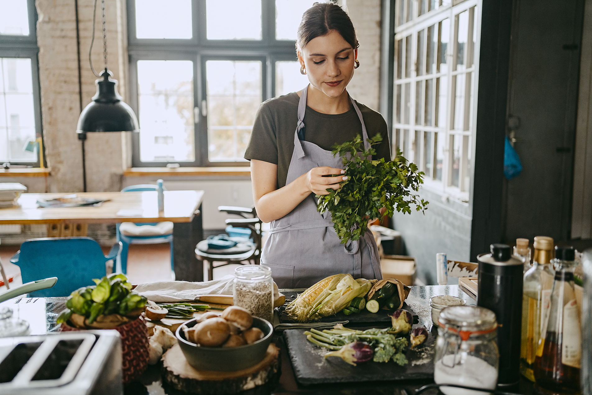Female chef wearing apron doing quality check of cilantro standing in studio kitchen, stock image, royalty-free, plant based food, vegetarian, vegan, sustainable, healthy eating,