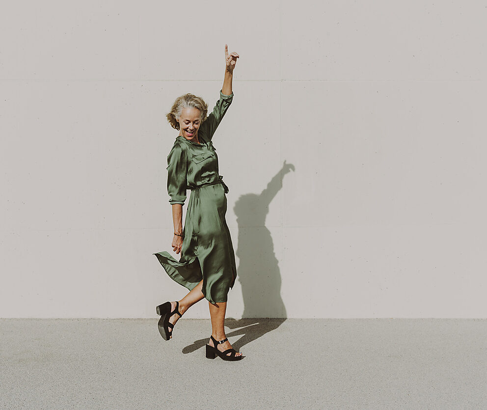 Happy woman dancing with hand raised on footpath, royalty-free, visual trends 2023, stock photography, communication