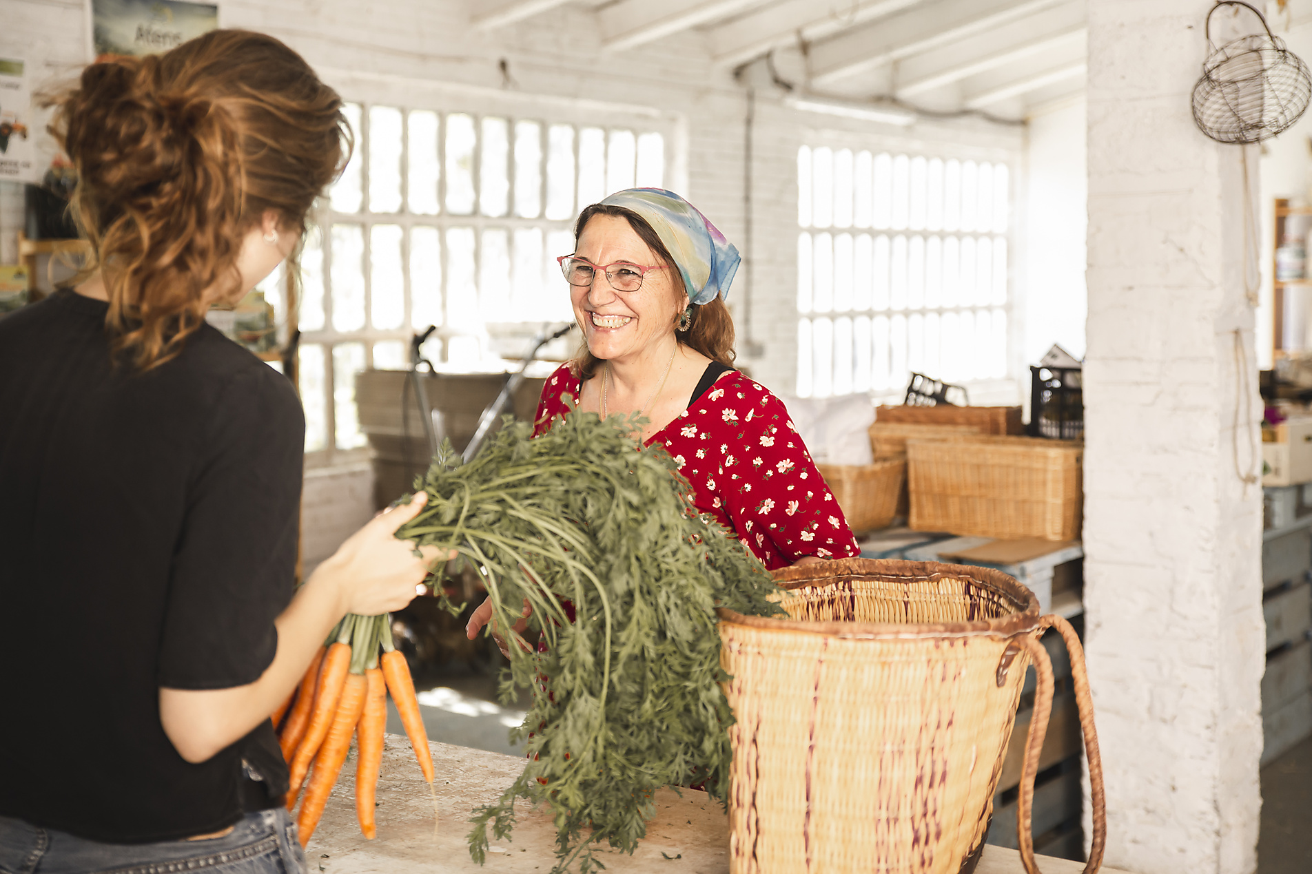 Happy customer talking with grocer holding carrots in shop, stock image, royalty-free, plant based food, vegetarian, vegan, sustainable, healthy eating