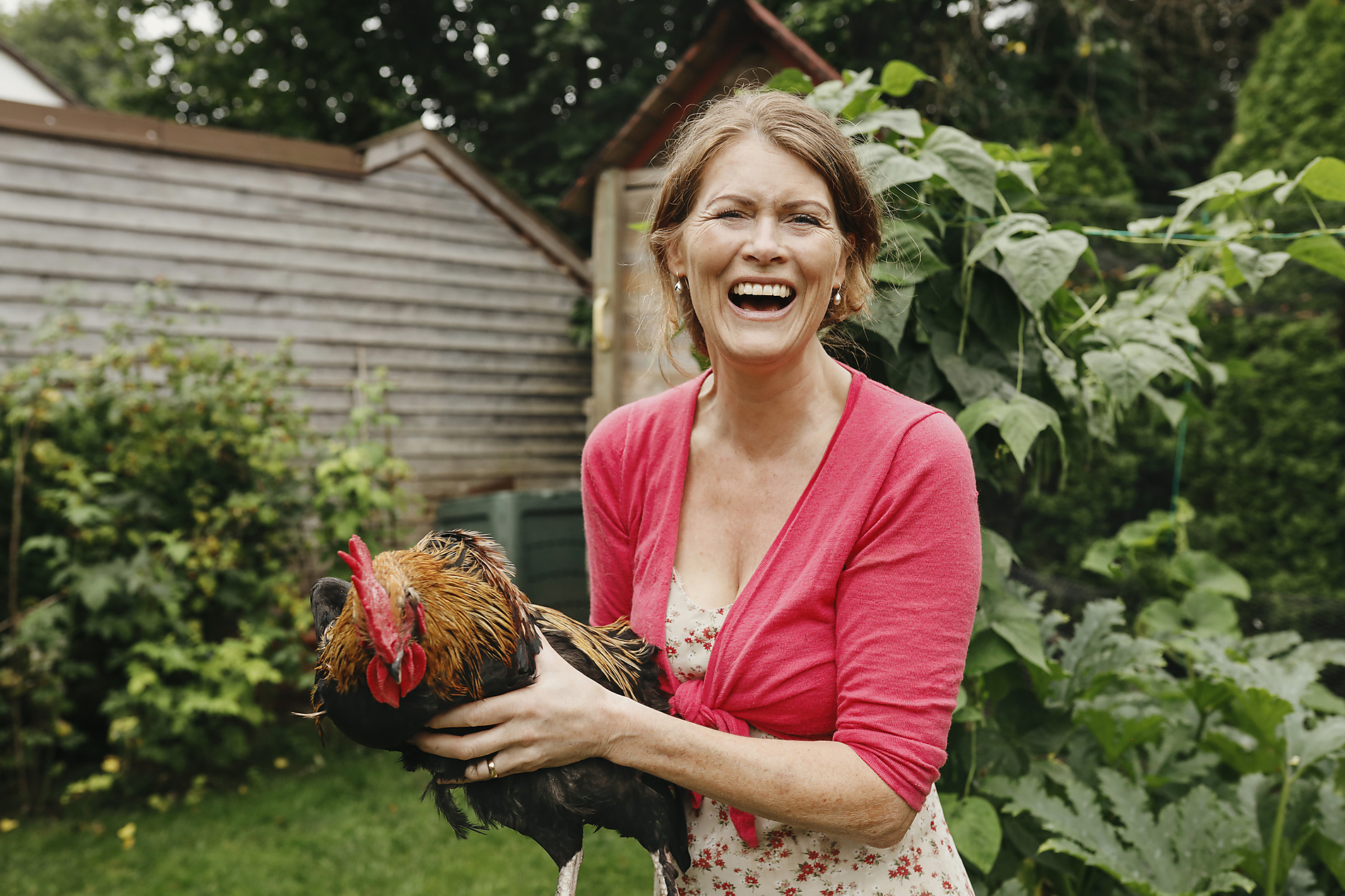 Mature woman laughing while carrying a rooster in the backyard, self-care, sustainability, optimism for action, stock photo, royalty free, Westend61, trends 2023,