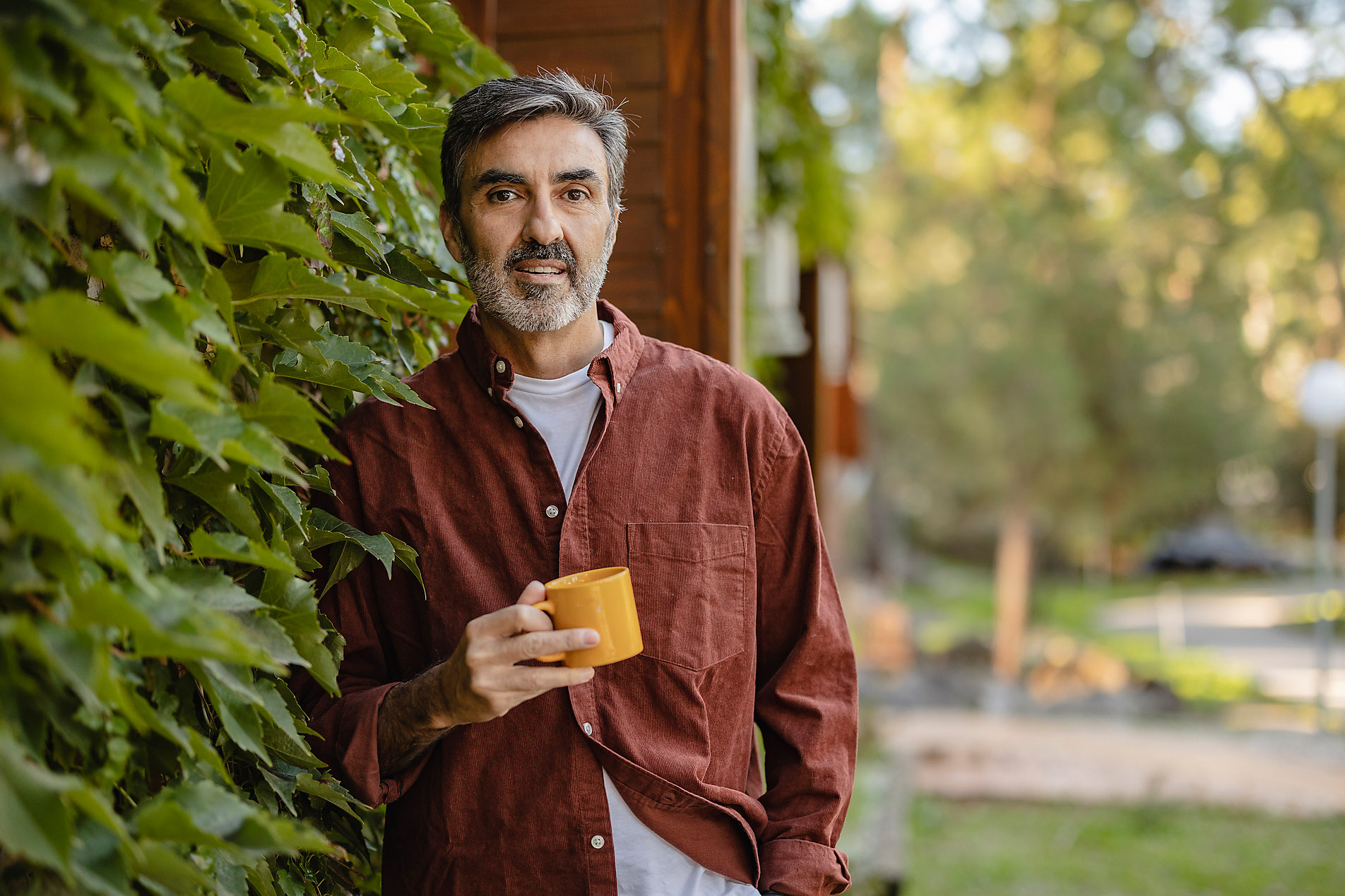 Elderly man holding coffee cup on facade with plants, sustainable architecture, westend61, stock image, royalty-free