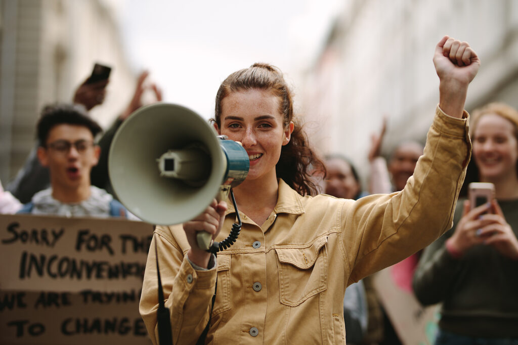 Modern urban woman protesting at a strike yelling her grievances into a megaphone. Female activist protesting with megaphone during a strike, stock image, royalty-free, optimism for action, sustainability, better future, vision, imagination