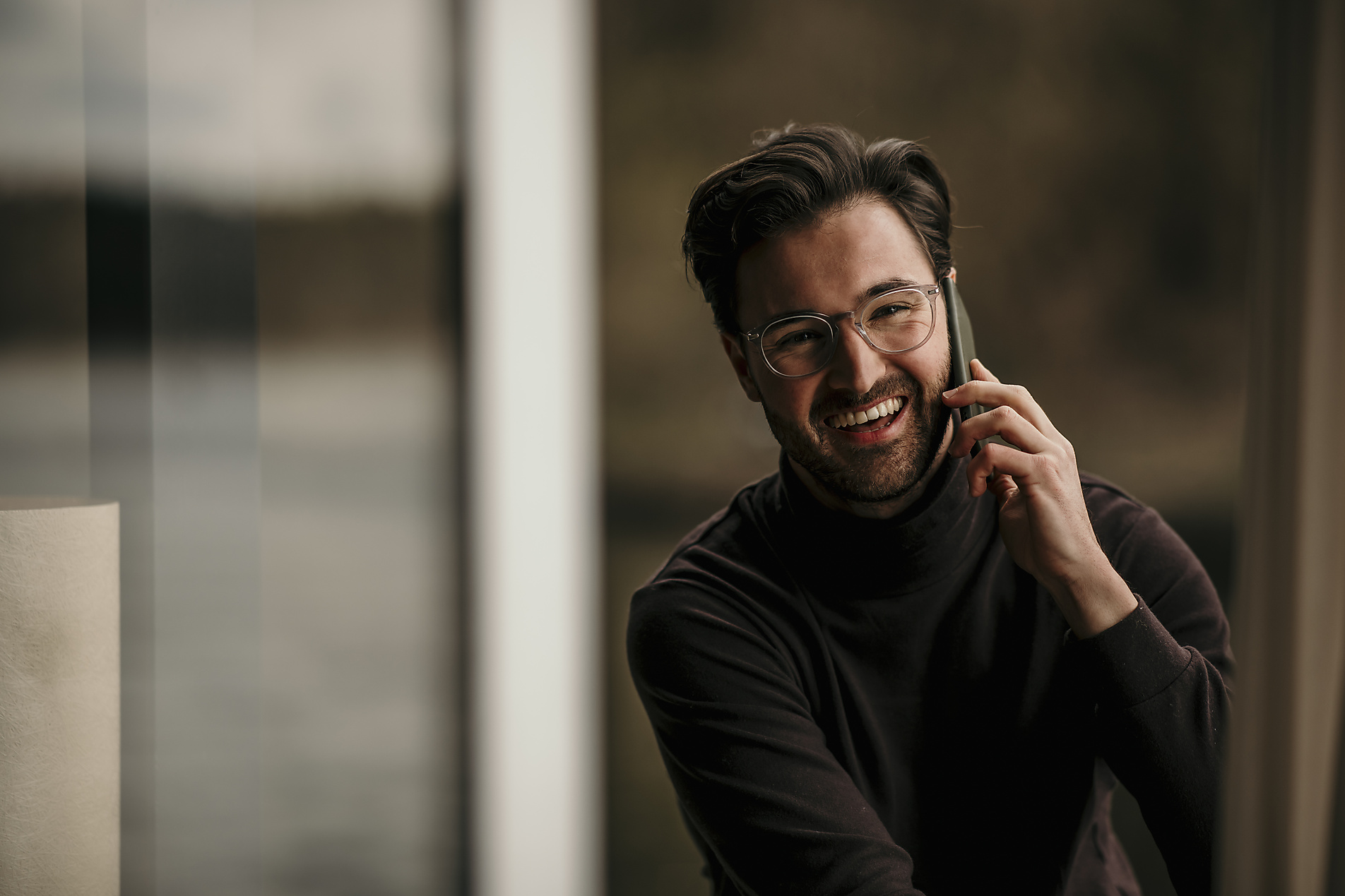 Happy man talking on mobile phone while looking through window, stock image, royalt-free, westend61, Malte Jäger