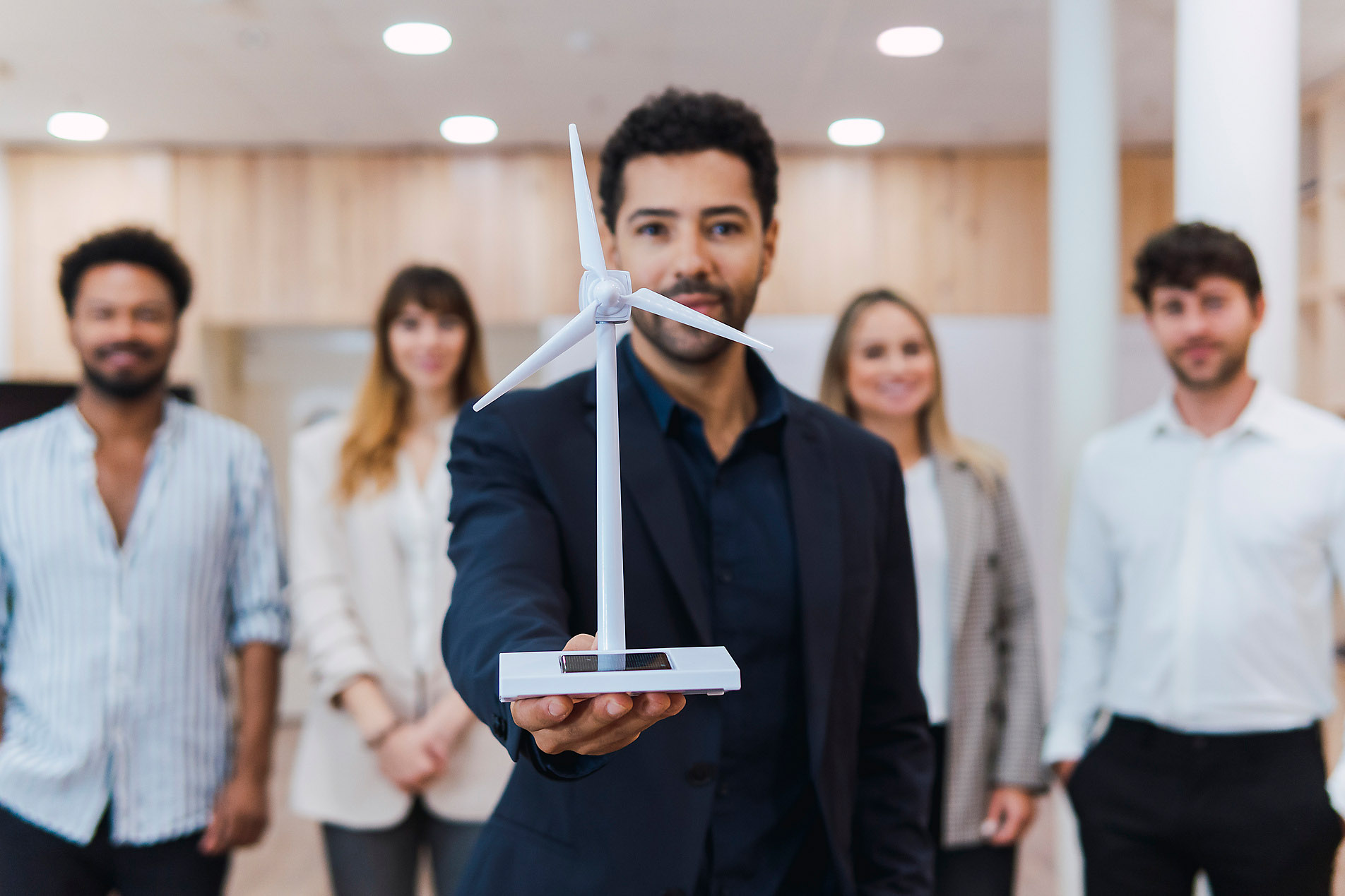 Businessman holding wind turbine model in front of his team in office, stock photo, royalty free, sustainability, architecture, renewable energy, wind energy, stock photo, royalty free, Westend61, Pau Novell