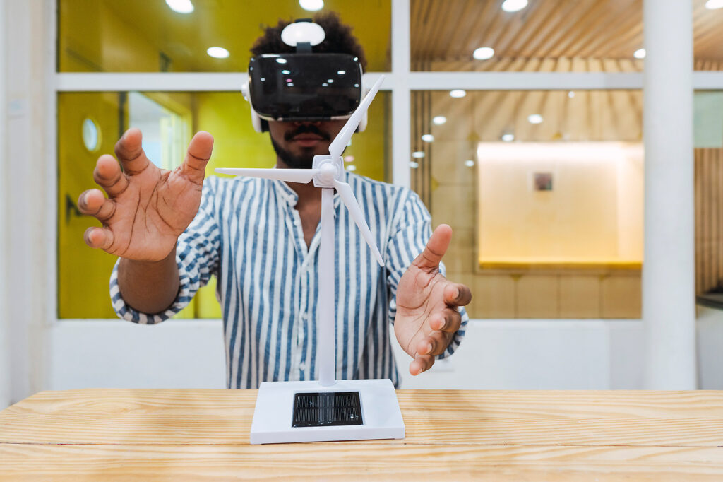 Engineer with wind turbine model on table in office with VR glasses, stock photo, royalty free, renewable energy, sustainability, wind energy