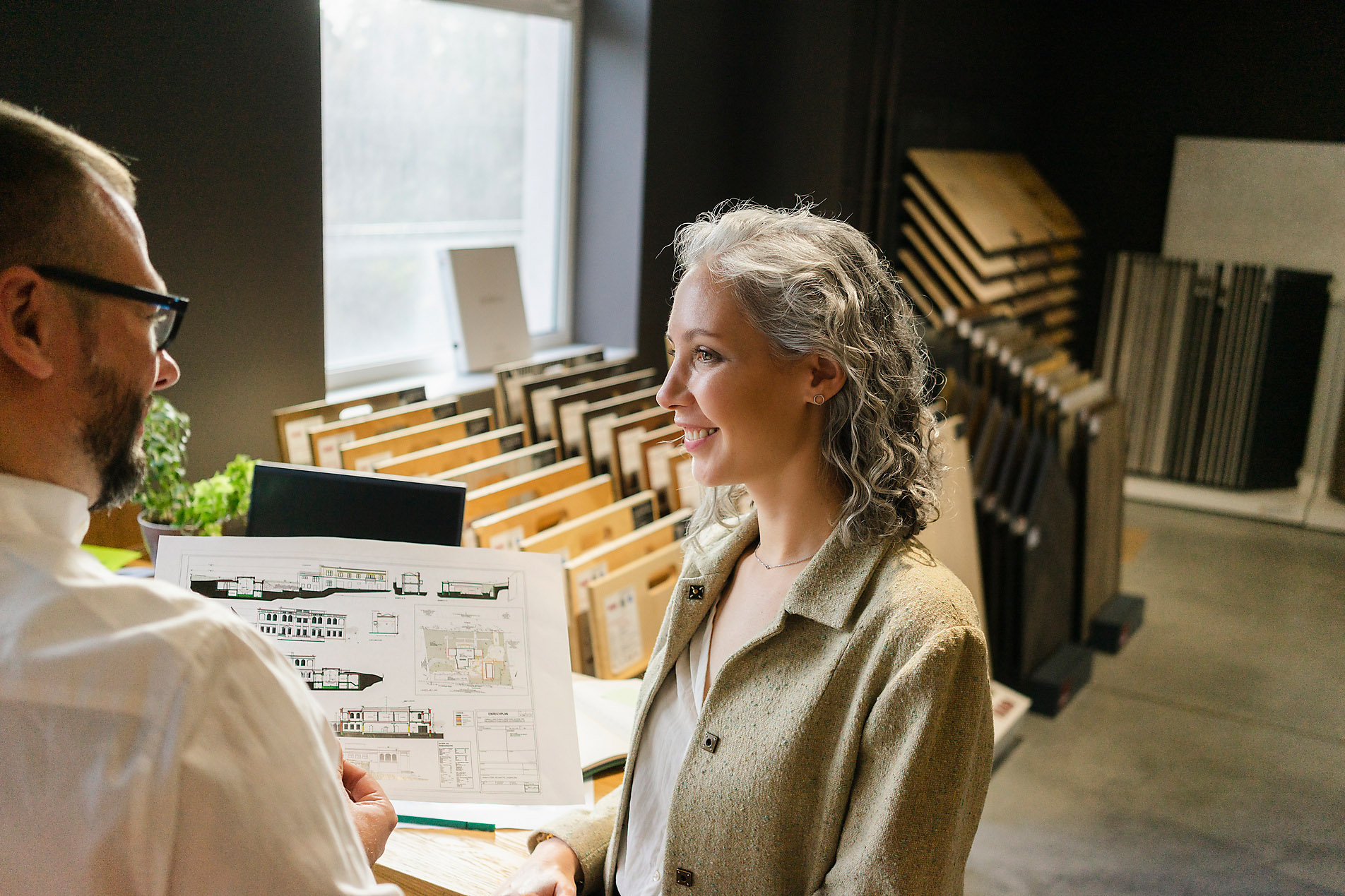 Smiling businesswoman looks at a colleague holding a blueprint in an architecture office, stock photo, royalty free, sustainability, newcomer, shoot club,