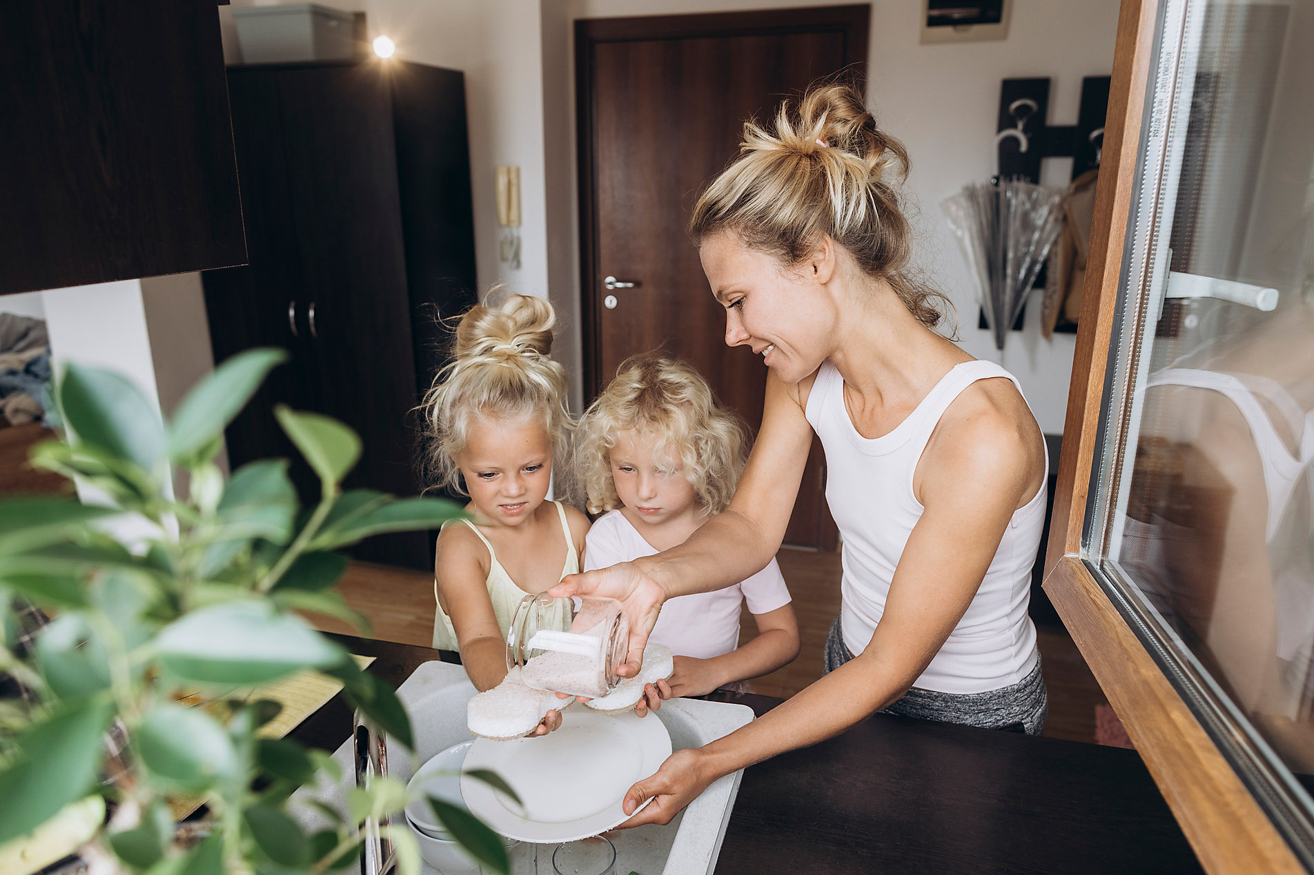 Woman with daughters washing dishes with salt in the kitchen, sustainability, green living, stock image, royalty-free