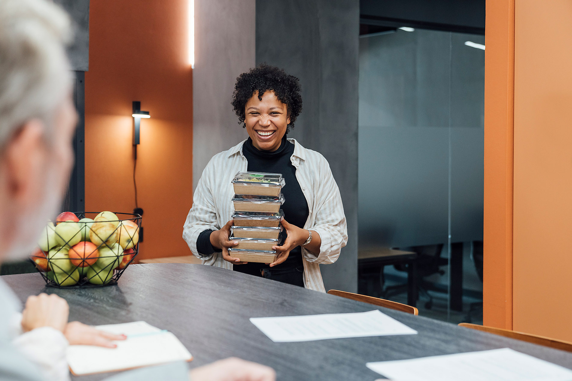 Happy young woman with take away lunch boxes standing by table in office, plant-based eating, healthy eating, sustainable office, stock image, royalty-free