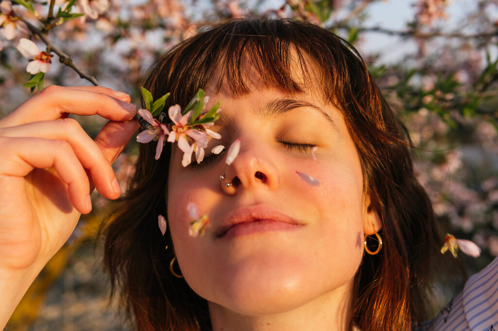Smiling woman holding almond blossom branch by eyes during sunset, Spring, season, spring, spring awakening, spring cleaning, nature, blossom, sunshine, change, new beginning, stock photo, royalty-free, Westend61