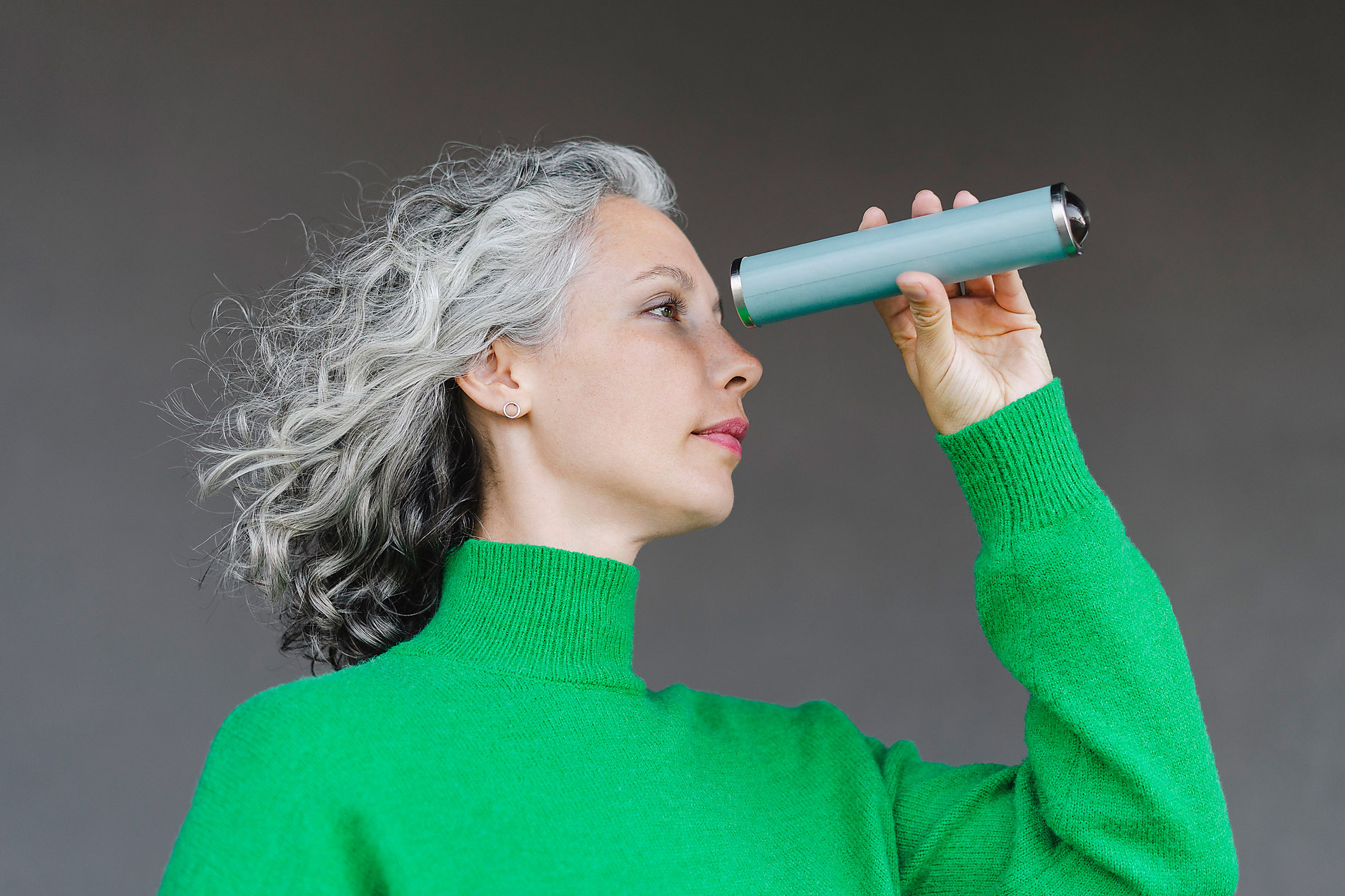 Stockfoto, lizenzfrei, echte Bilder, authentische Bilder, Lebendigkeit, Frau mit lockigem grauem Haar schaut durch ein Monokular vor einer Wand, VISTA Kollektion