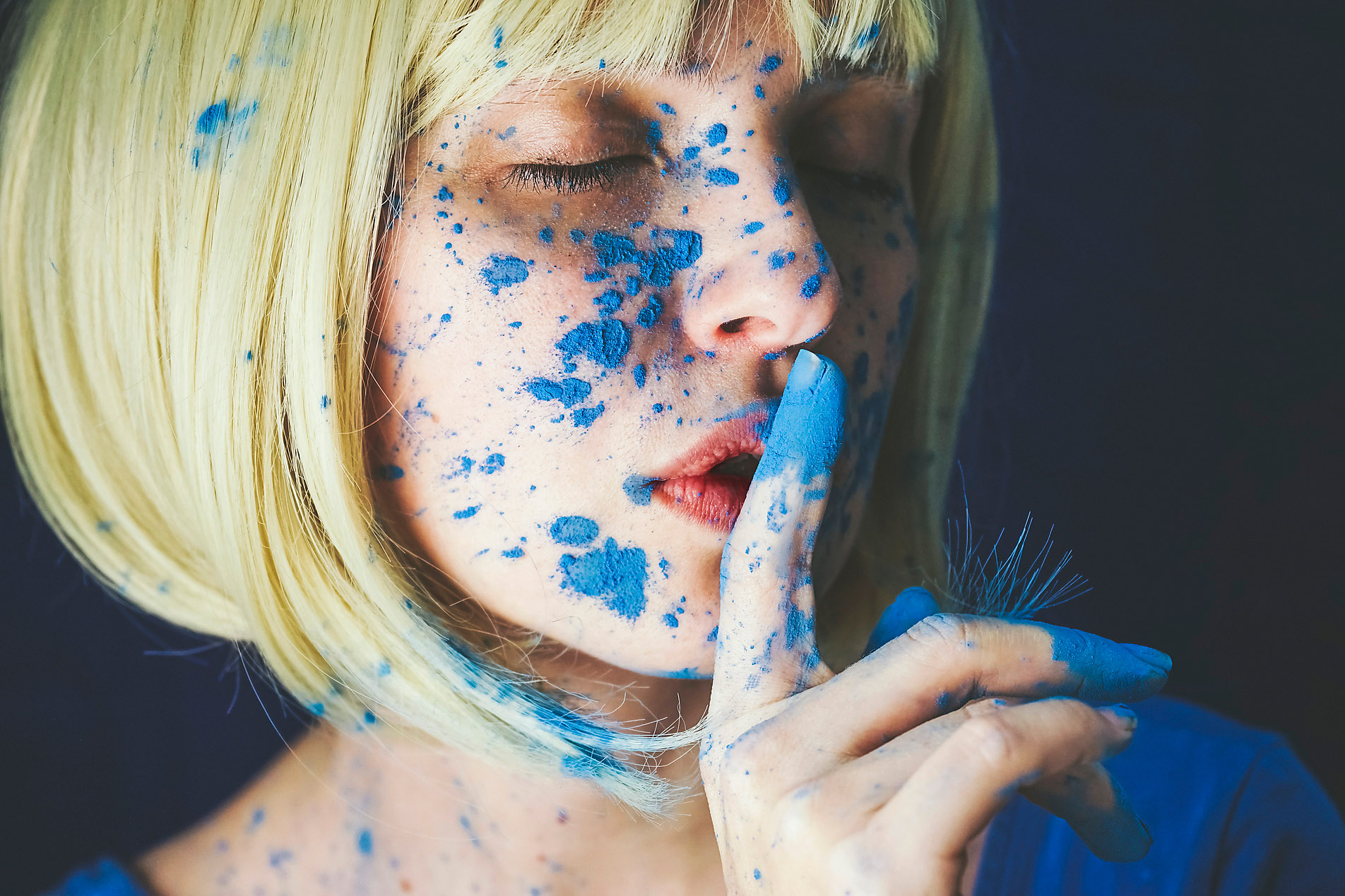 Frau mit blauer Puderfarbe und Finger auf den Lippen vor schwarzem Hintergrund, Westend61, VISTA Kollektion, echte Bilder, authentische Bilder, Farbe, Blau