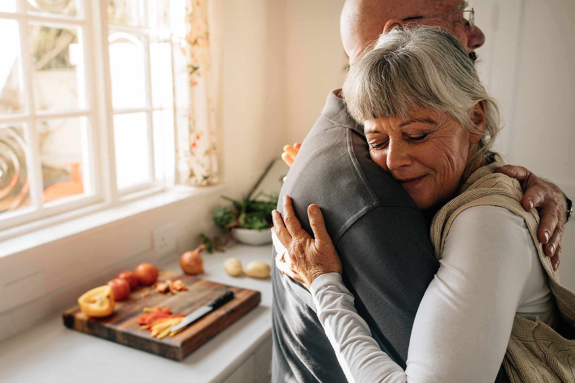 Stockfoto, lizenzfrei, Liebe im Alter, Senioren, Lovestory Seitenansicht eines älteren Paares, das sich zu Hause umarmt. Ältere Frau umarmt ihren Mann mit geschlossenen Augen in der Küche stehend, Jacob Lund, Westend61, Stockfotografie