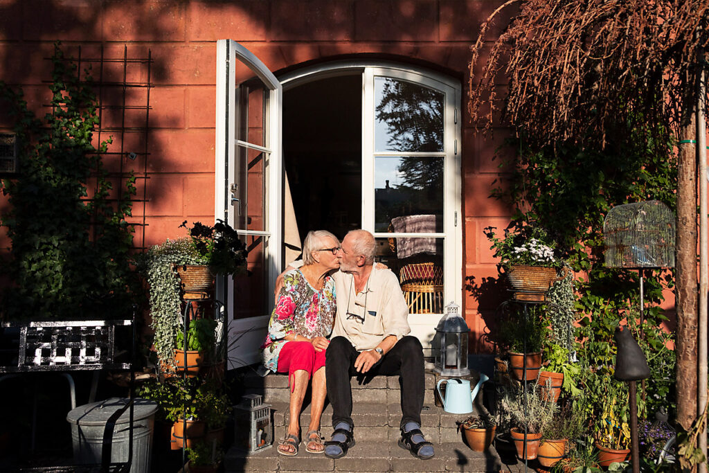 Elderly couple sitting in front of their house kissing, love, senior love story, westend61, silver ager, best ager, digit ager, target audience