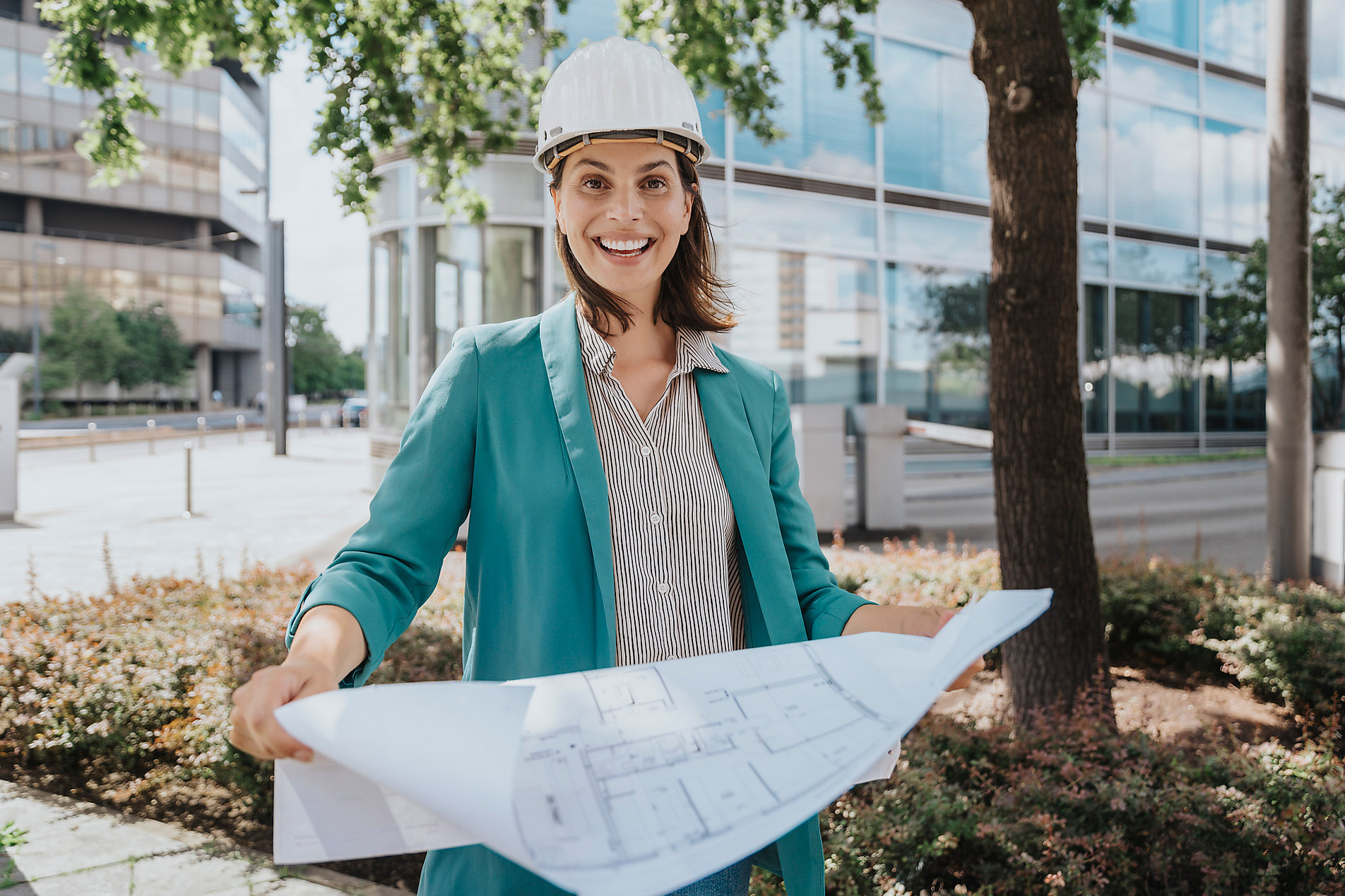 Happy architect wearing hardhat standing with construction plan