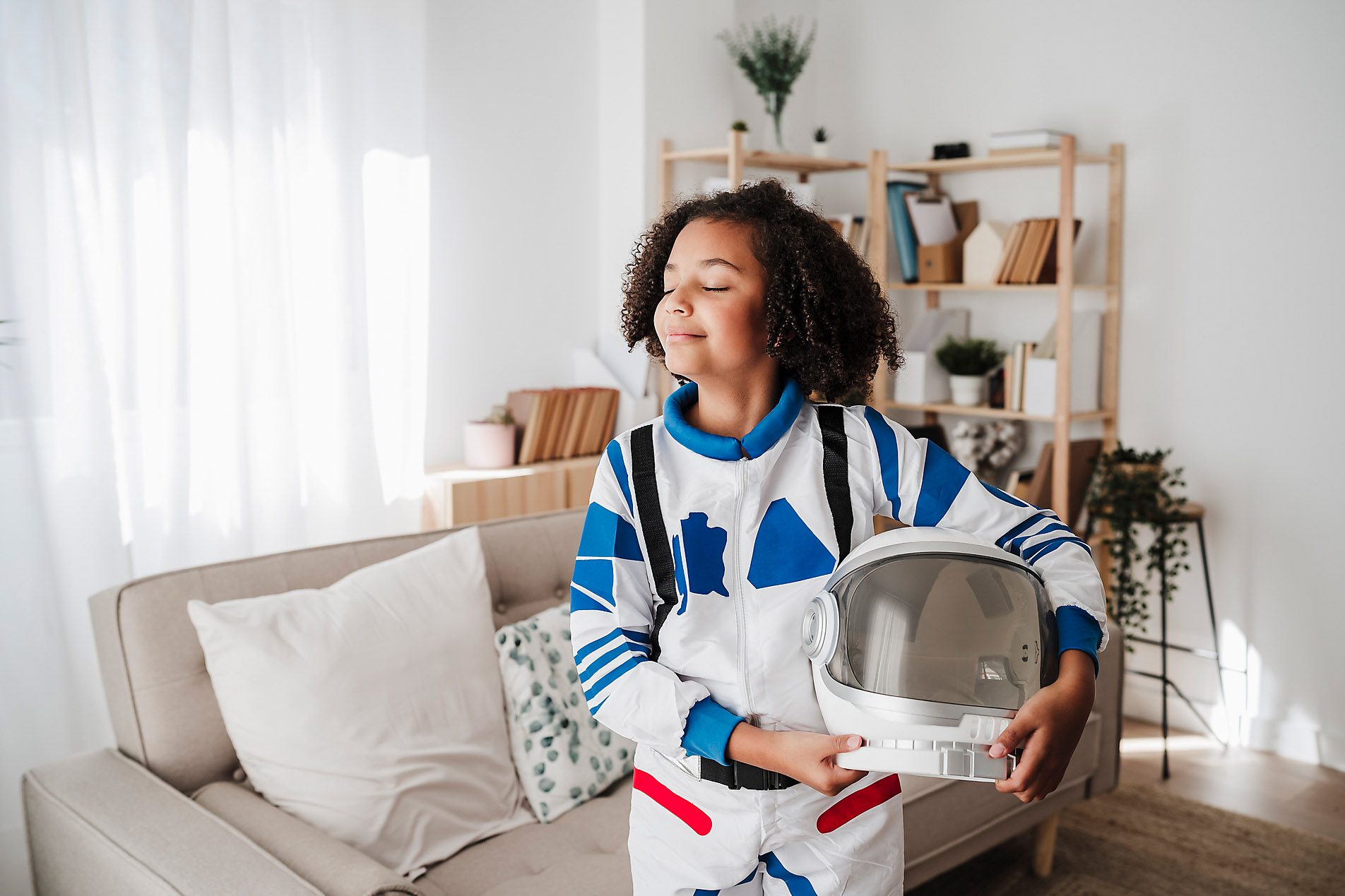 Smiling girl wearing space suit standing with eyes closed at home, stock image, royalty-free, future, vision, dreams, inspiration, imagination, Westend61, Eva Blanco