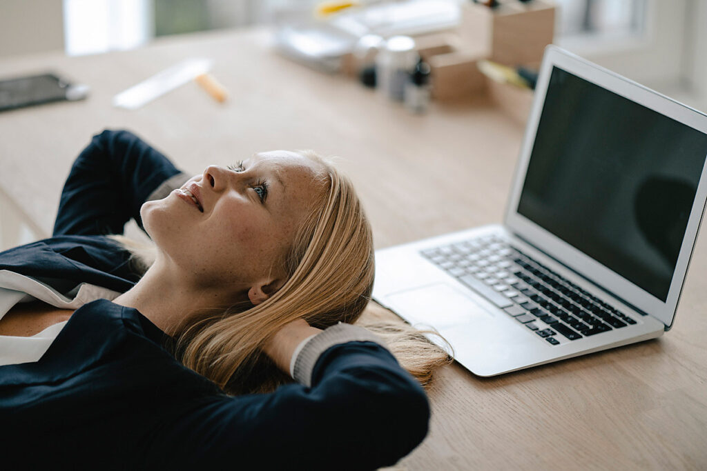 Young businesswoman having a break in office lying on desk, stock image, royalty-free, future, vision, imagination, new work, mindfulness, business development