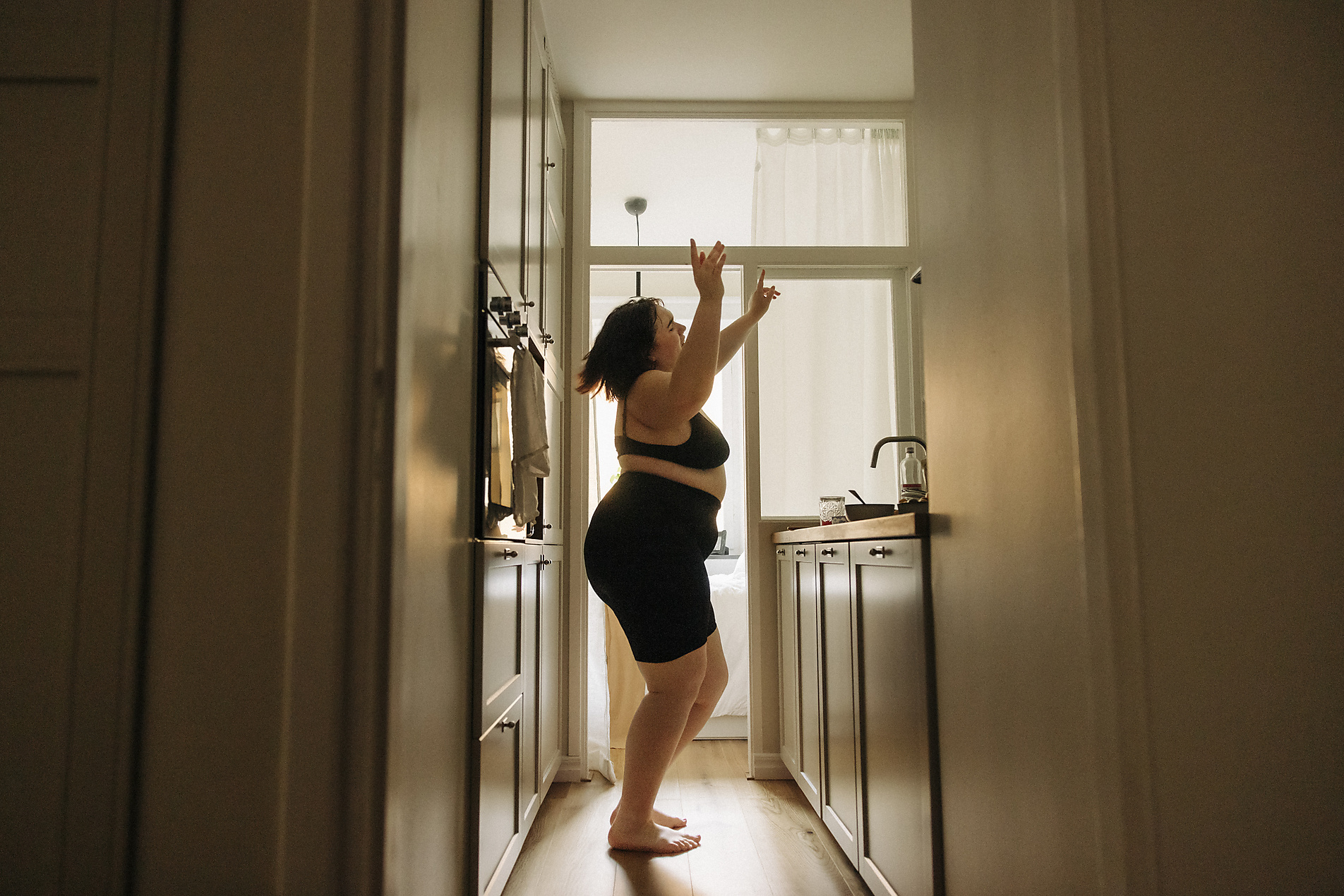 Royalty Free Stock image of young voluptuous woman with arms raised enjoying dance in kitchen