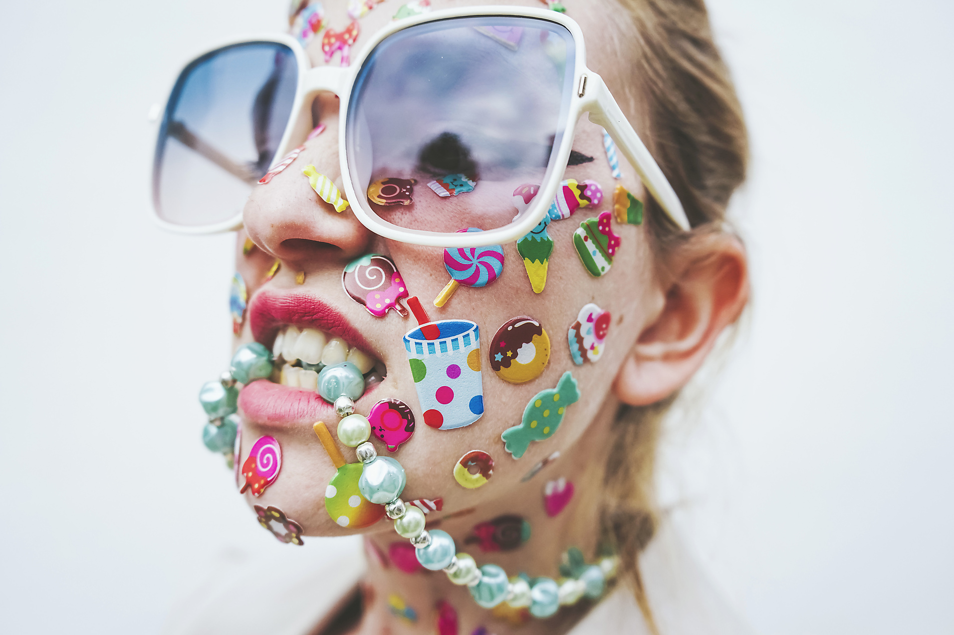 Royalty Free Stock Image of woman with multi colored stickers on face biting necklace in front of white background