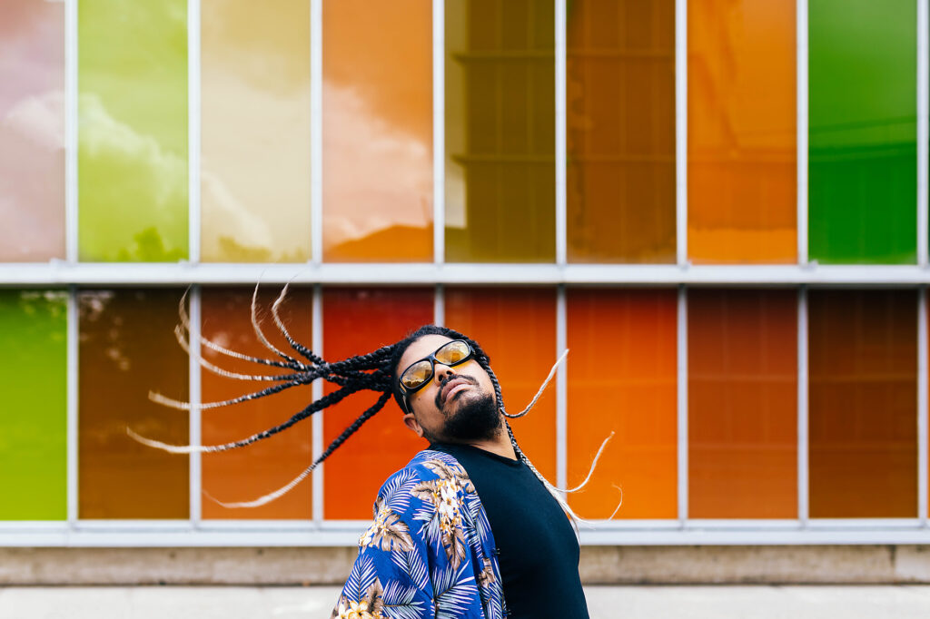 Latin man with long braids tossing his hair back, wearing sunglasses and a blue shirt against a colorful backdrop. Royalty free image Latin man with long braids tossing his hair back, wearing sunglasses and a blue shirt against a colorful backdrop.
Royalty free image