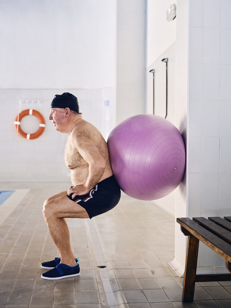 Side view of middle aged male swimmer doing squat exercises with fit ball during aerobics training in pool Stock Image Side view of middle aged male swimmer doing squat exercises with fit ball during aerobics training in pool Stock Image