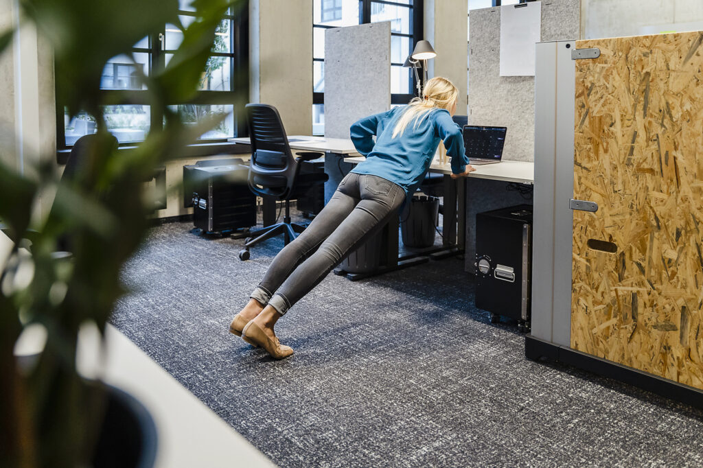 Young businesswoman doing push-ups on desk in office Stockphoto Young businesswoman doing push-ups on desk in office Stockphoto