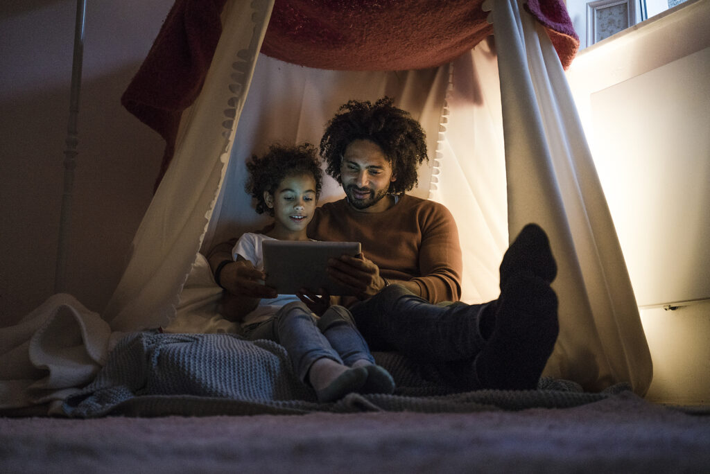 Father and daughter sitting in dark children's room, looking at digital tablet
Royalty free image