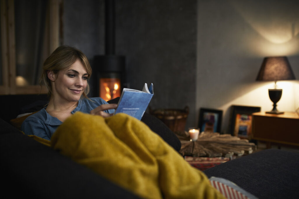 Porträt einer lächelnden Frau, die abends zu Hause auf der Couch ein Buch liest
Lizenzfreies Stockfoto