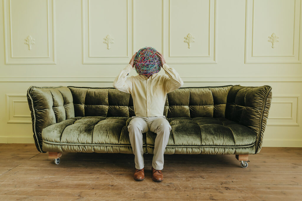 Man holding mask of chaotic thoughts and sitting on sofa near wall Royalty-free image Man holding mask of chaotic thoughts and sitting on sofa near wallRoyalty-free image