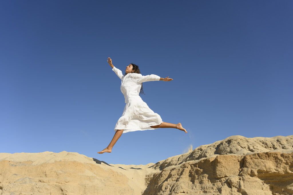 Frau in weißem Kleid springt in einer Wüstenlandschaft unter klarem blauem Himmel Lizenzfreies Stockfoto Frau in weißem Kleid springt in einer Wüstenlandschaft unter klarem blauem HimmelLizenzfreies Stockfoto