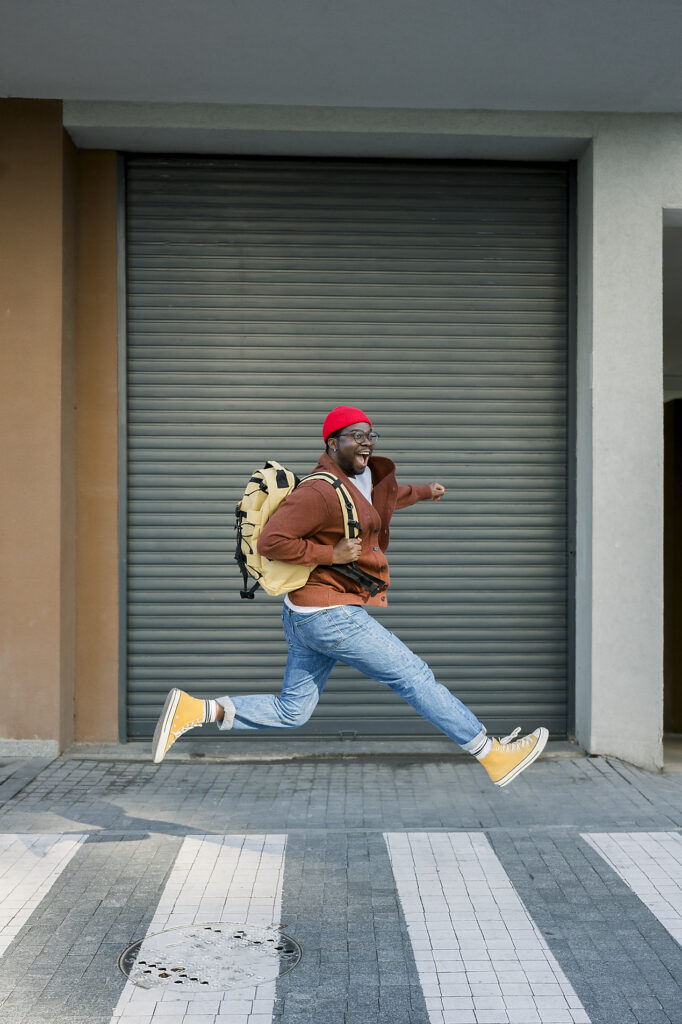 Fröhlicher Mann mit Rucksack in Freizeitkleidung auf städtischer Straße Lizenzfreies Stockfoto Fröhlicher Mann mit Rucksack in Freizeitkleidung auf städtischer StraßeLizenzfreies Stockfoto
