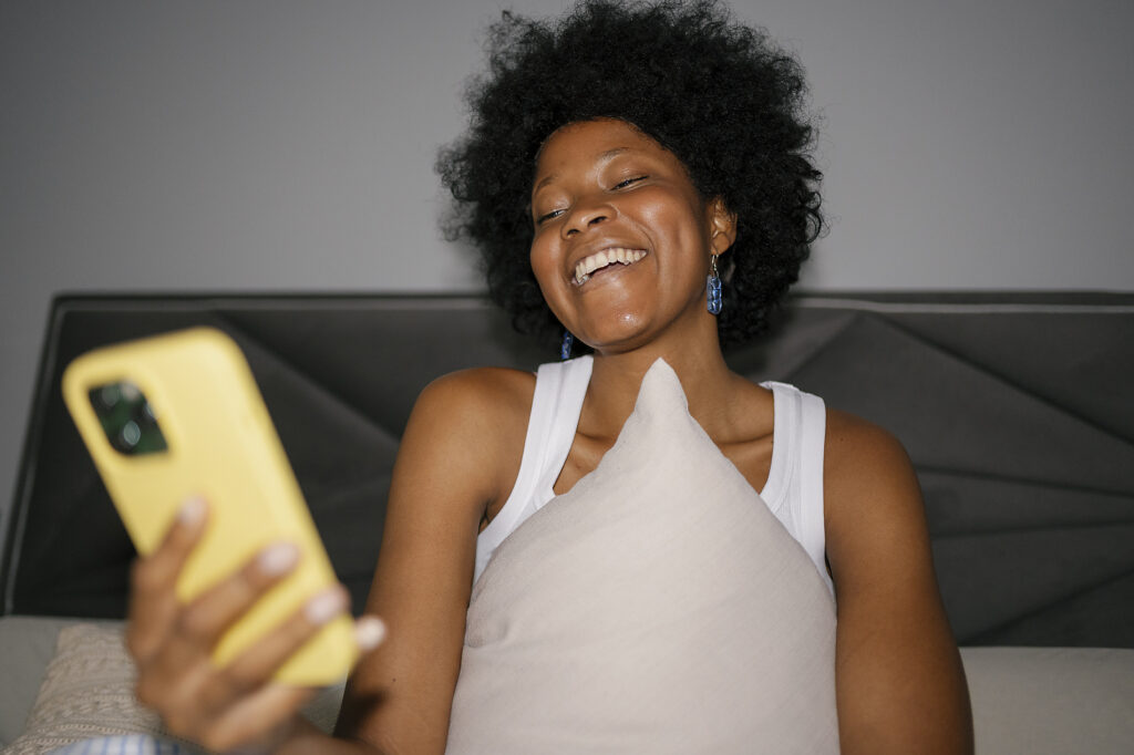 Fröhliche Frau lacht und benutzt Smartphone im Bett Lizenzfreies Stockfoto Fröhliche Frau lacht und benutzt Smartphone im BettLizenzfreies Stockfoto