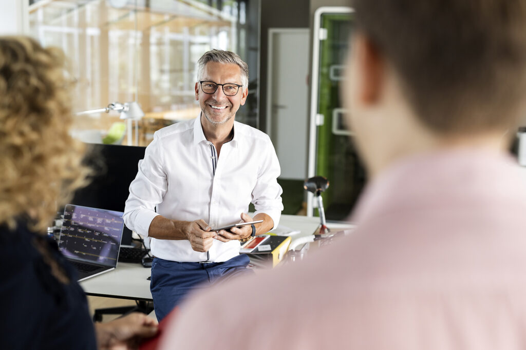 Ein lächelnder Geschäftsmann, der ein Tablet in der Hand hält, während er sich im Büro mit Kollegen unterhält Lizenzfreies Stockfoto Ein lächelnder Geschäftsmann, der ein Tablet in der Hand hält, während er sich im Büro mit Kollegen unterhält
Lizenzfreies Stockfoto