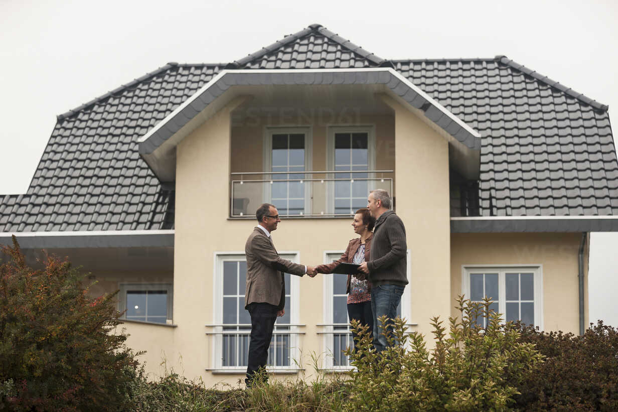 Estate agent shaking hands with potential buyers in front of residential house stock photo