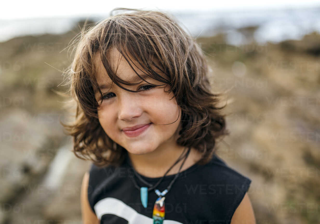 Spain, Gijon, portrait of smiling little boy with brown hair at rocky coast  stock photo