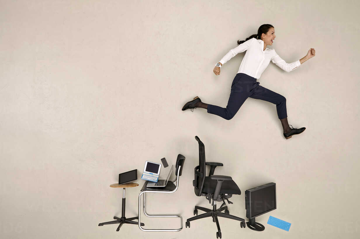businesswoman-jumping-over-chairs-and-devices-stock-photo
