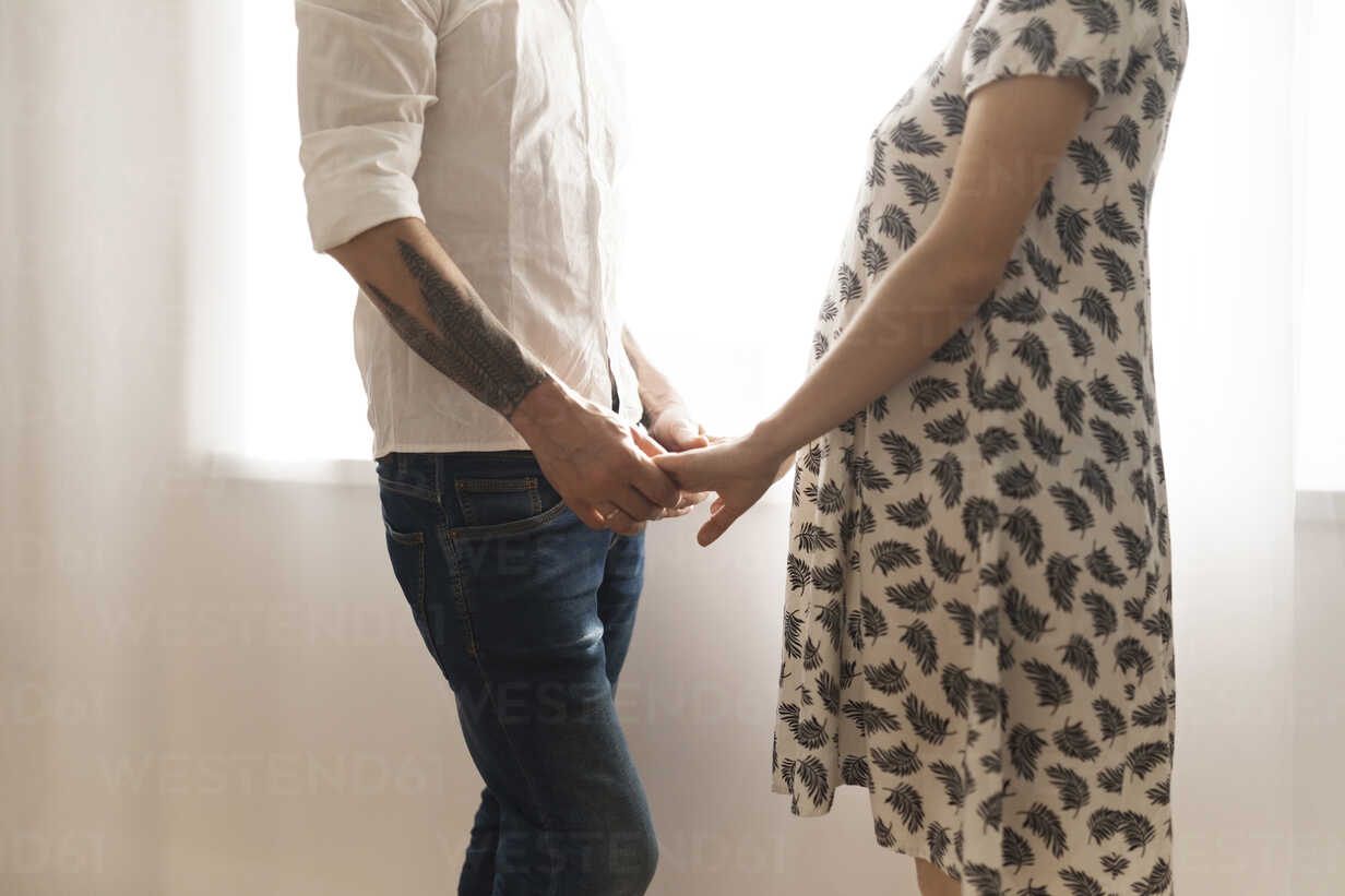 Midsection of man holding PRegnant woman's hand while standing at home stock photo