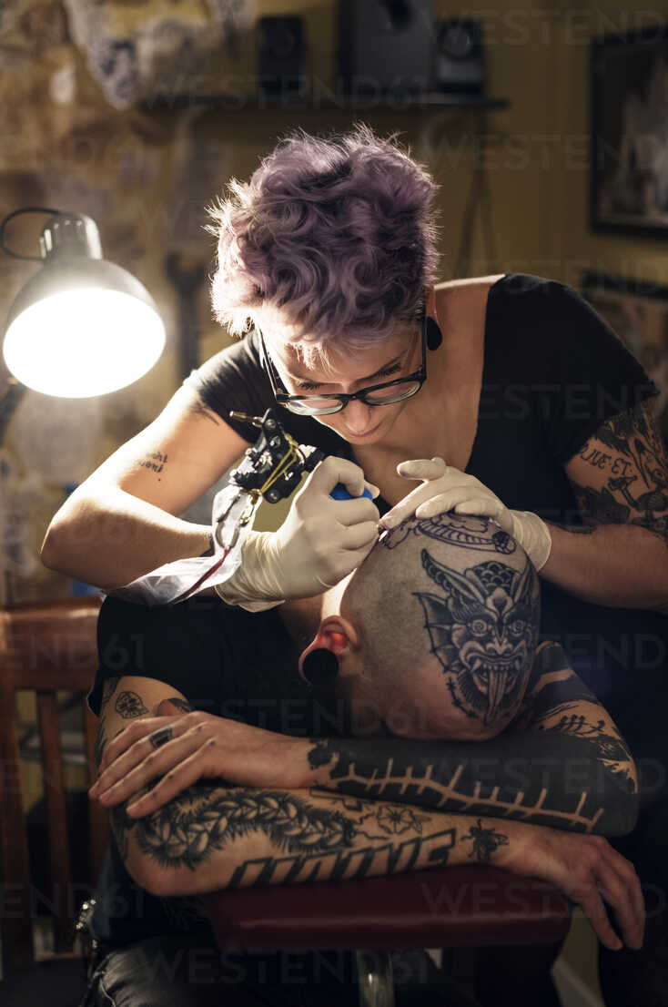 Female tattoo artist tattooing male client in studio stock photo