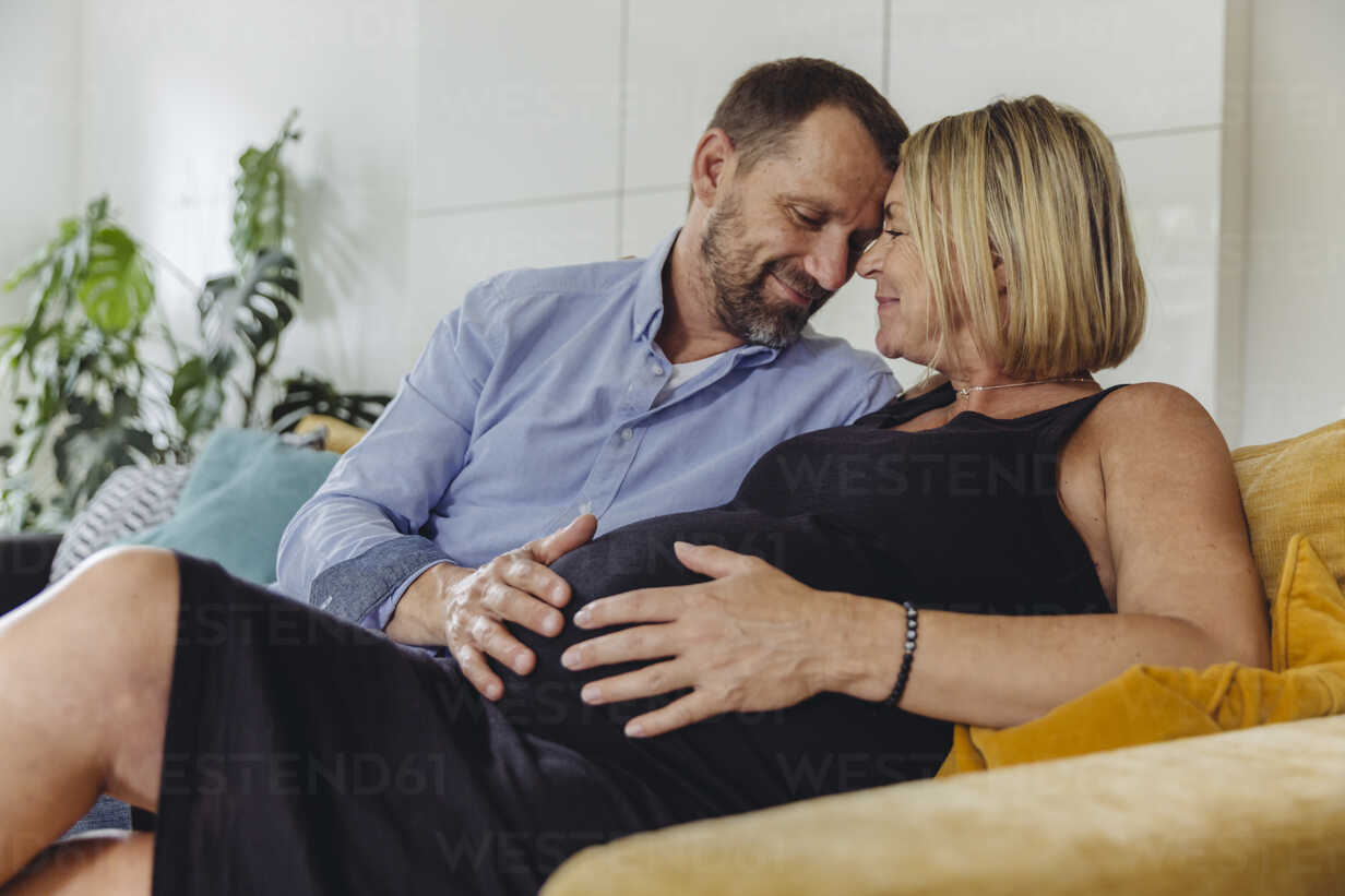 Mature wife com Mature Man And His Pregnant Mature Wife Sitting On Couch Touching Her Belly Stockphoto